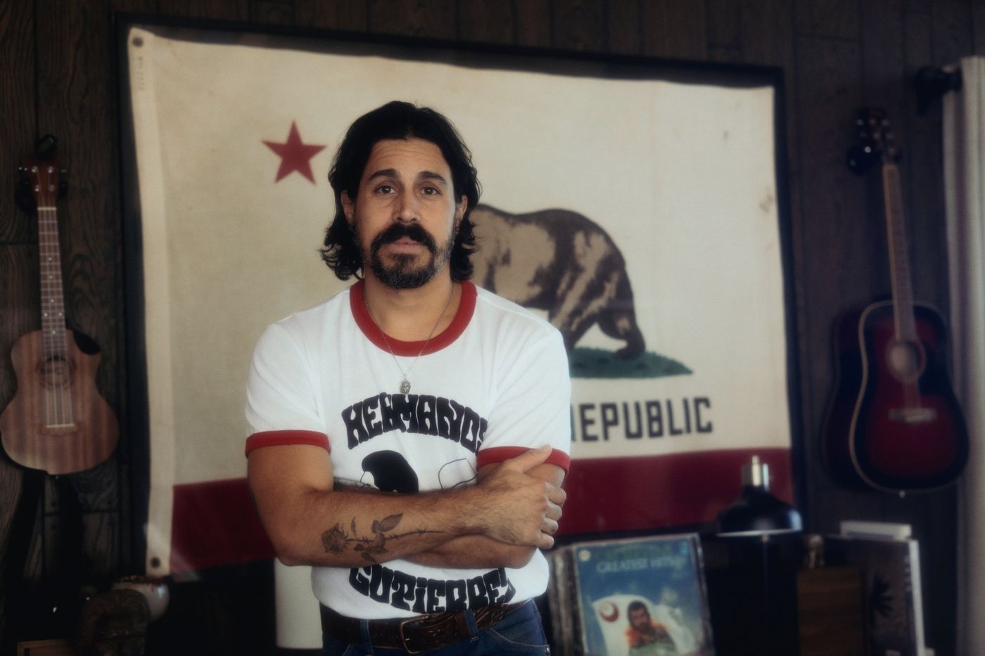 Coquí standing with his arms crossed in front of a vintage California flag